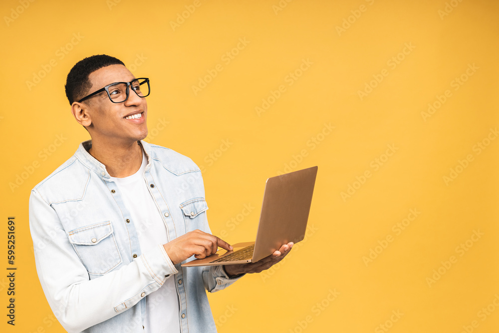 Young smiling african american man standing and using laptop computer isolated over yellow background. Young smiling african american man standing and using laptop computer isolated over yellow background.