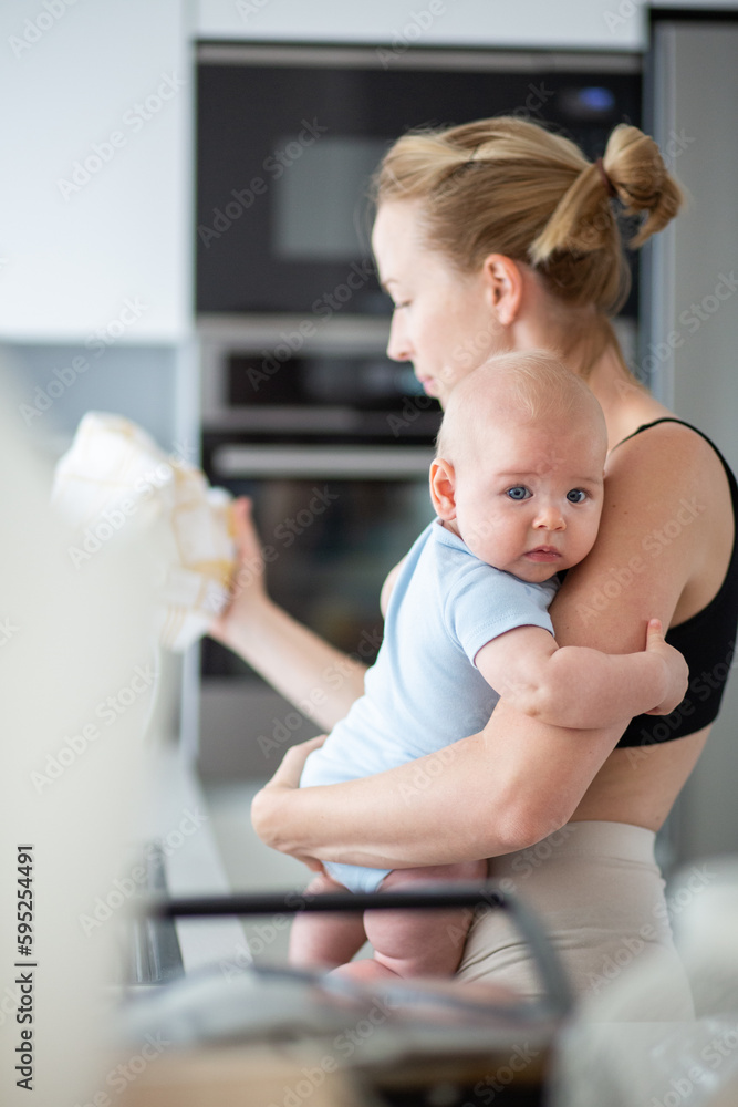 Woman wiping kitchen sink with a cloth after finishing washing the dishes while holding four months old baby boy in her hands. Woman wiping kitchen sink with a cloth after finishing washing the dishes while holding four months old baby boy in her hands.