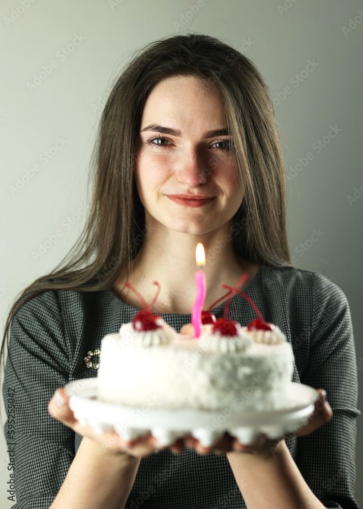 A beautiful girl with a cake in her hands. It's her birthday. White cake, studio shot. Making a birthday wish. A modest holiday A beautiful girl with a cake in her hands. It's her birthday. White cake, studio shot. Making a birthday wish. A modest holiday