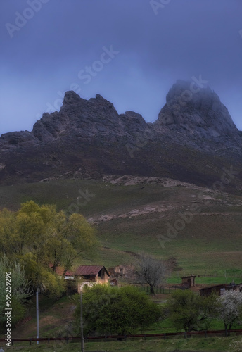 old village at the foot of the mountains with bizarre peaks in the fog