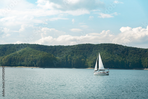 Tranquil scene with a sailing boat on a calm lake with forest hills in the background. Recreational boating on the lake in summer