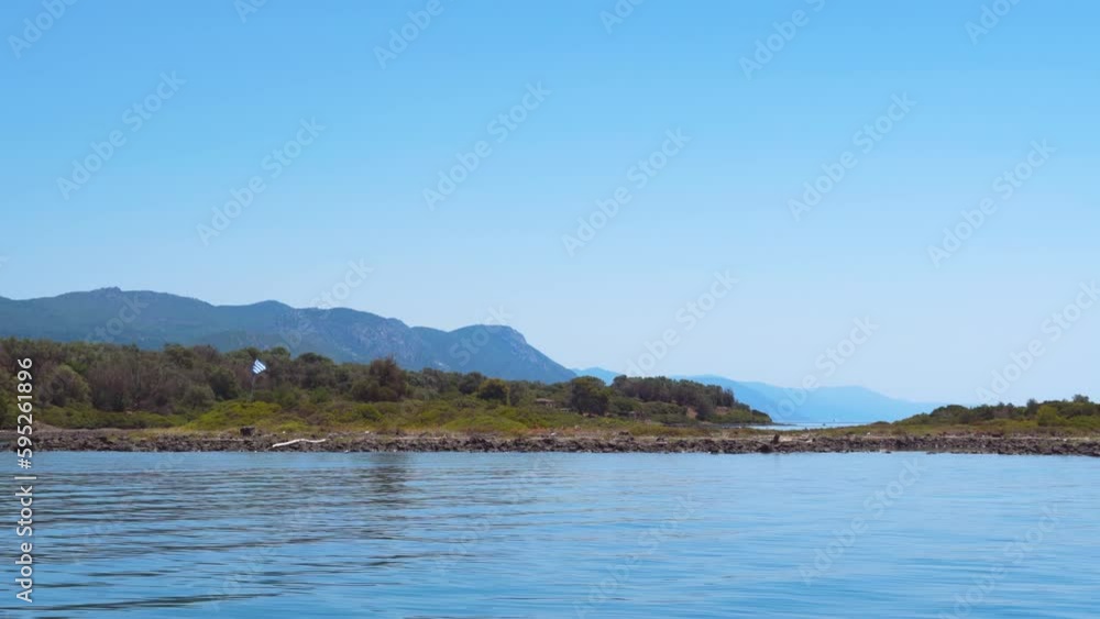 Sailing ship day side POV view looking to a rocky coastline island strip with green vegetation and a Greek flag waving on the far end. Sailing ship day side POV view looking to a rocky coastline island strip with green vegetation and a Greek flag waving on the far end.