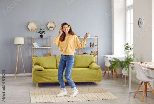 Overjoyed girl wearing headphones listening to music and dancing. Happy positive girl in casual clothes having fun and relaxing in living room at home. Woman enjoying music and leisure weekend © Studio Romantic
