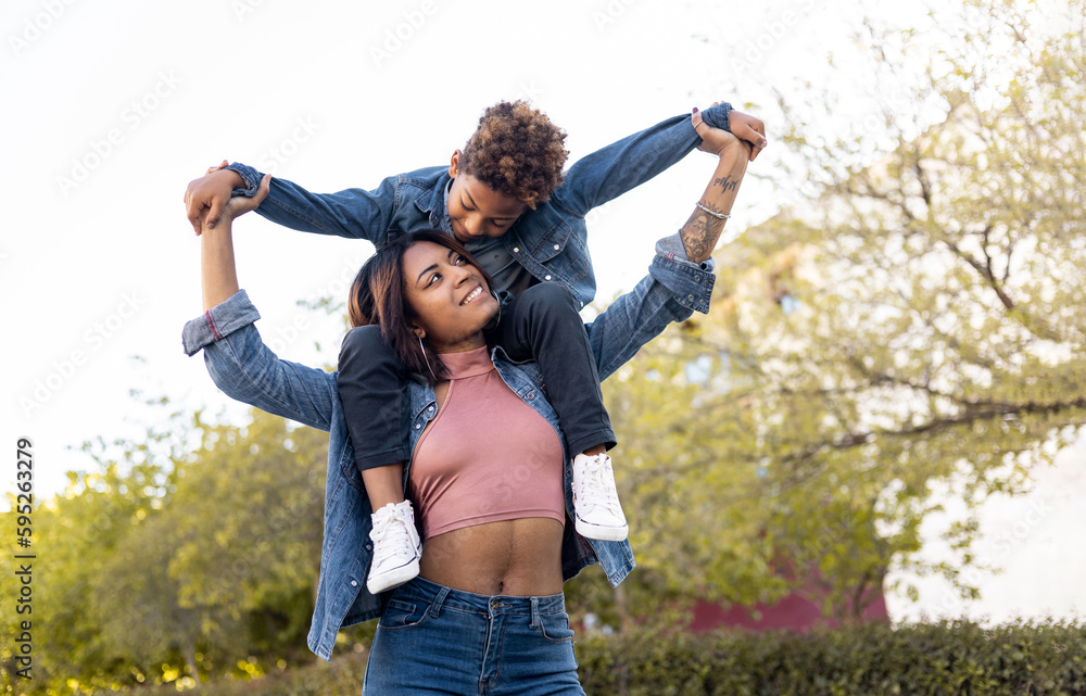 Two darkskinned brothers are in an outdoor park. The straighthaired girl carries her brother