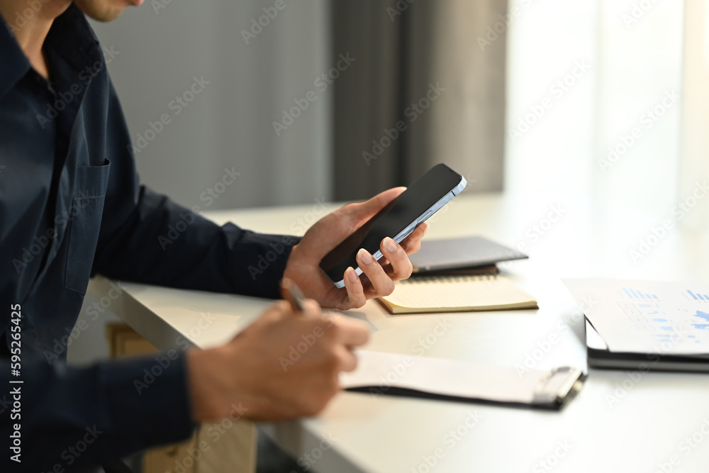 Adult businessman using smartphone and making notes on paper. People, Technology and Communication Adult businessman using smartphone and making notes on paper. People, Technology and Communication