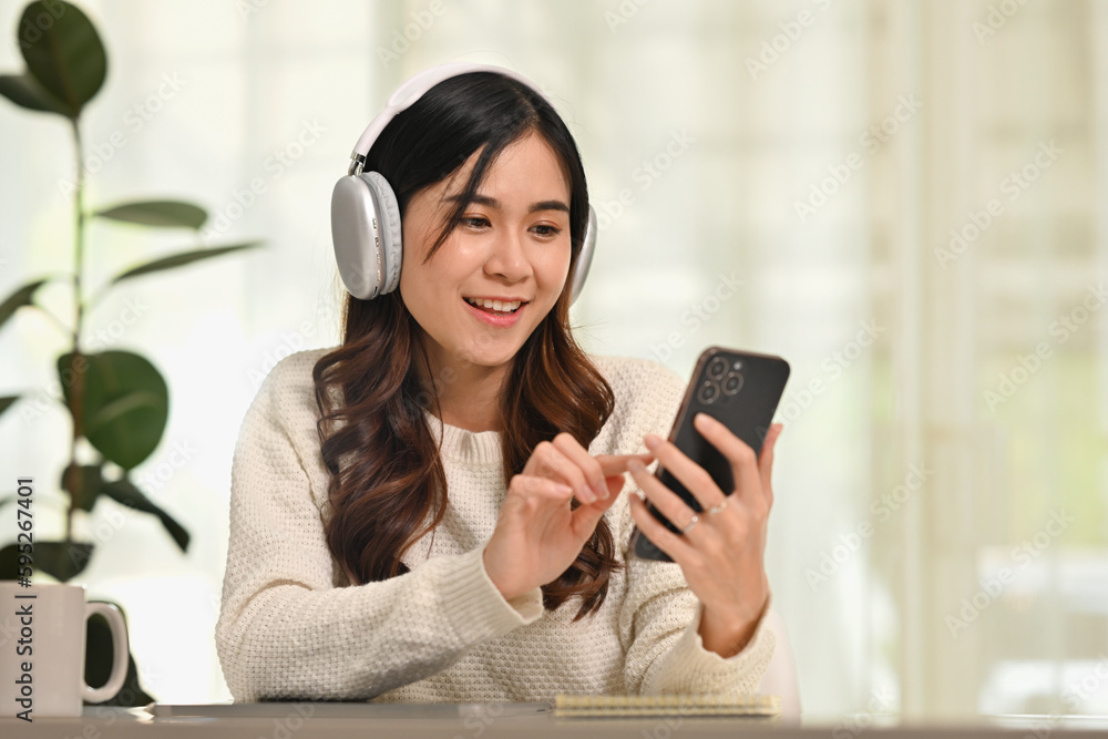 Happy millennial woman wearing modern wireless headphones and using smartphone. People, technology and lifestyle