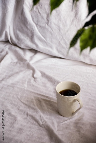 Steaming hot morning coffee resting on a bed, with a green leaf visible in the frame