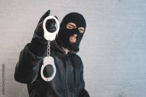 bandit in a black mask and gloves with handcuffs in his hands on a white background. Release from imprisonment. Prison break concept. Jailbreak