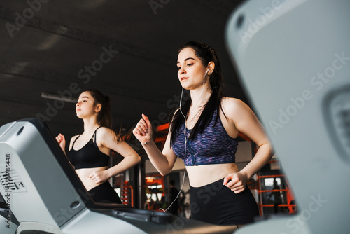 Young pretty sporty girl trains her muscles in the gym by running on a treadmill. © Olha