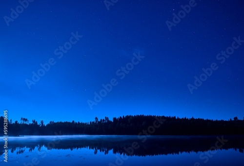 Tranquil evening sky is mirrored in a still pond, glowing with the reflection of stars in the dark © Pekka/Wirestock Creators