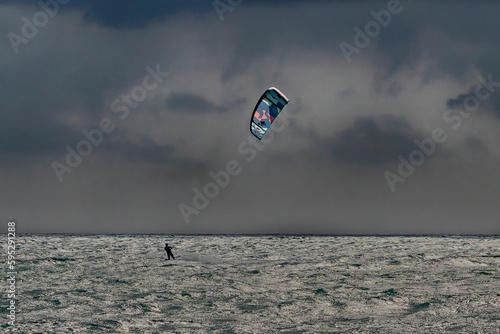 Person riding a windsurfing board with a parachute in the sky above them.