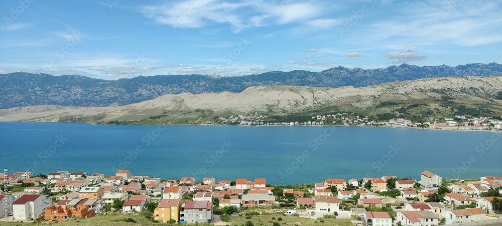 A sea between two landscapes with houses. In the background are mountains and the sky is blue and slight cloudy.