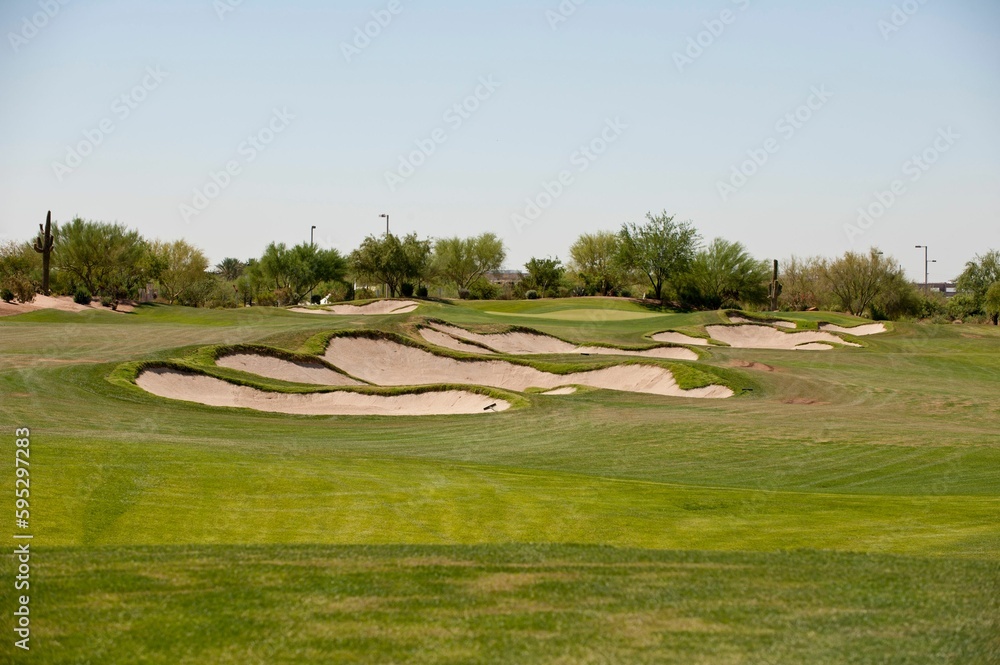 Scenic landscape featuring a lush green golf course with sand bunkers scattered across the fairway