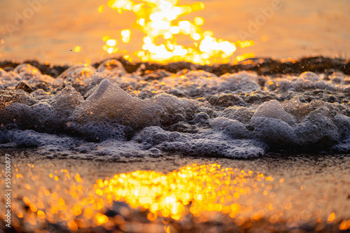 The photo of the waves crashing into the shore during the setting sun, the waves and the light are bokeh.