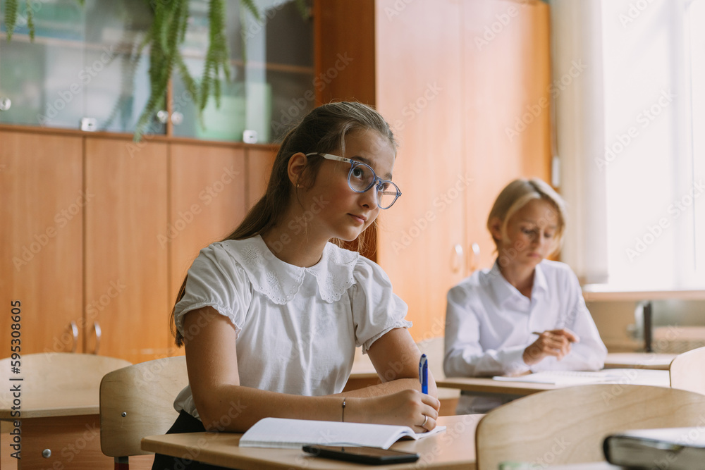 teen students writing in copybook at desk in classroom, working on lesson teen students writing in copybook at desk in classroom, working on lesson