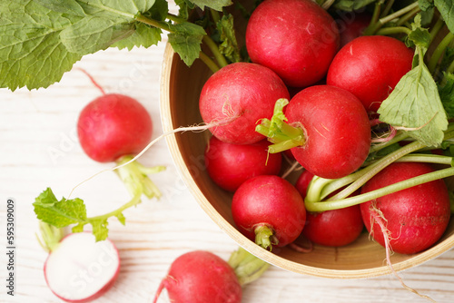 Ripe red radish in a bowl on a wooden background, top view, closeup. Fresh red radish..
