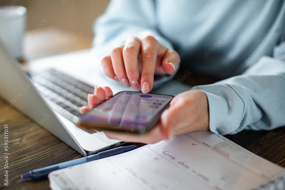 Fototapeta premium Young adult woman using a banking app on her phone while working from home