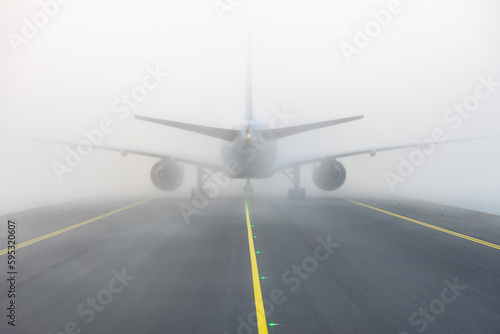 Airplane taxing on taxiway in white fog conditions. Yellow taxi line photo