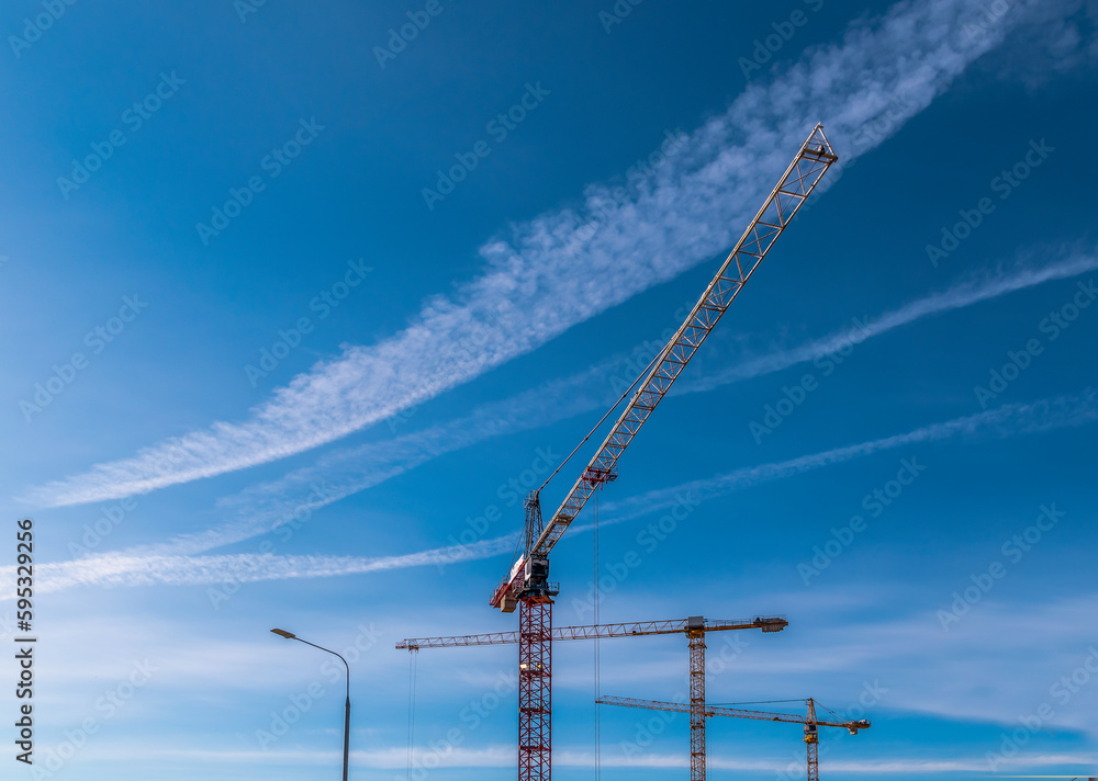 Construction cranes on a background of blue sky with white clouds Construction cranes on a background of blue sky with white clouds