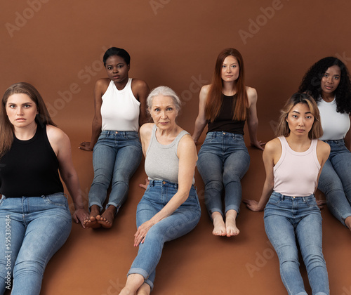 Six different females on a brown background. Group of six women with different body types and skin tones are looking at camera. Females of different ages in casuals sitting together in studio. photo