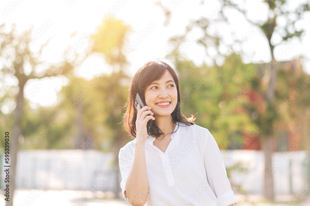 Portrait beautiful young asian woman with smart mobile phone around outdoor nature view in a sunny summer day Portrait beautiful young asian woman with smart mobile phone around outdoor nature view in a sunny summer day