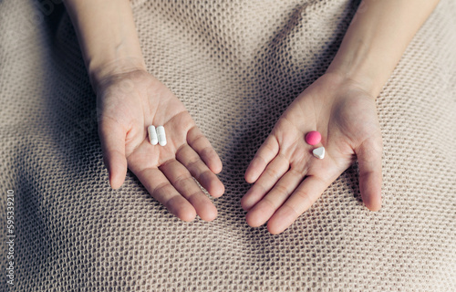 Female hands hold and offer two choice medicine pills capsule for chosen. White and pink candy or meds compare to choose from. Concept decision making or indecisiveness.