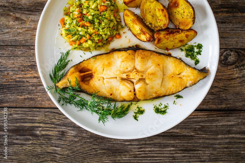 Fish dish - fried halibut with baked potatoes and cabbage salad on wooden table