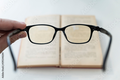 book and eye glasses for read and write over blurred background with copy space  reading glasses in his hands on a blurry book background. poor vision concept. loss of vision 