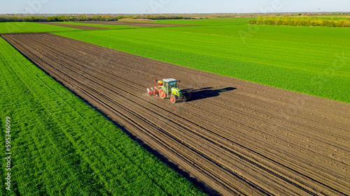 Aerial view of tractor as dragging a sowing machine over agricultural field, farmland