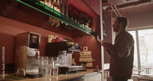 Male barkeeper checking quantity of alcohol bottles on shelves