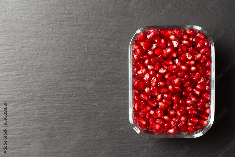 Pomegranate grains in a plate on a black background.