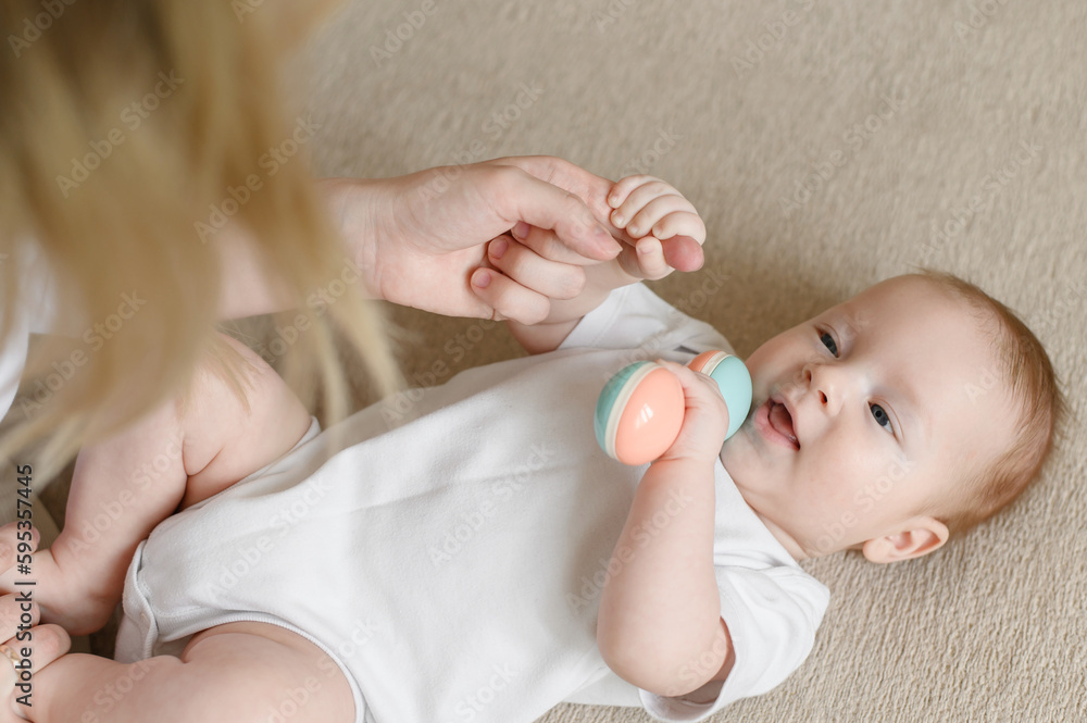 Happy mom and adorable baby are playing with a rattle. Toy for the development of fine motor skills of the baby.The concept of motherhood, maternity leave, care, childhood, children day, baby day Happy mom and adorable baby are playing with a rattle. Toy for the development of fine motor skills of the baby.The concept of motherhood, maternity leave, care, childhood, children day, baby day