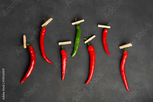 Composition of red and green peppers hung on pegs, one stand out. Isolated on black or dark gray background. Flat lay, top view.