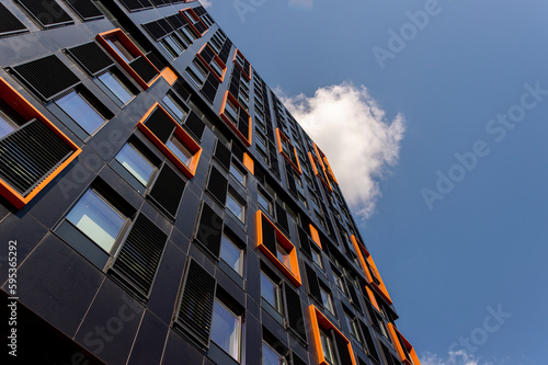 Modern black and orange building against a blue sky, looking up.