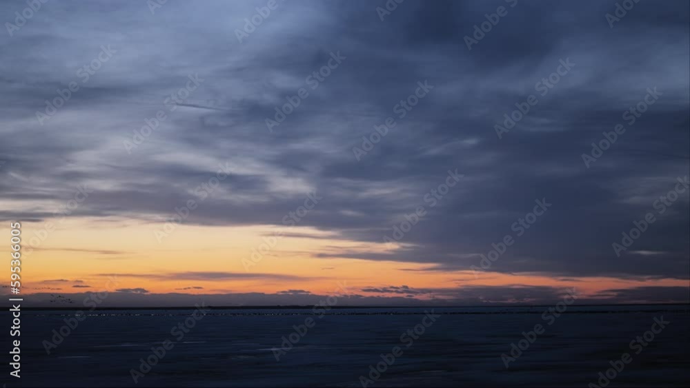 Sun setting above the frozen lake with a flock of birds flying in the distance. Slow motion. Sun setting above the frozen lake with a flock of birds flying in the distance. Slow motion.