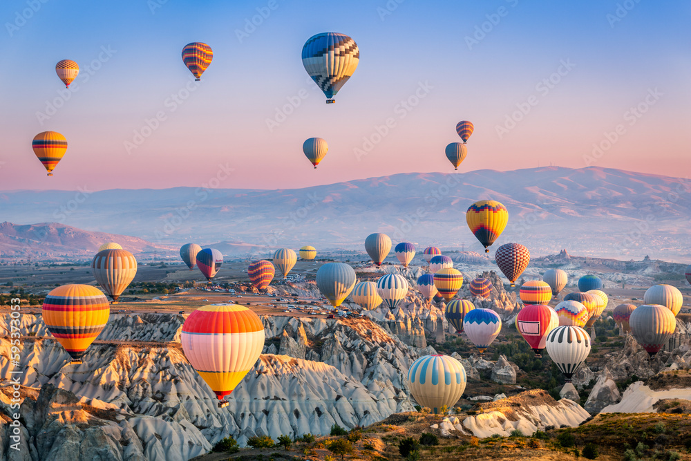 Aerial view of a fleet of hot air balloons, in Cappadocia, Turkey, at sunrise. Cappadocia is a popular tourist destination. - obrazy, fototapety, plakaty 