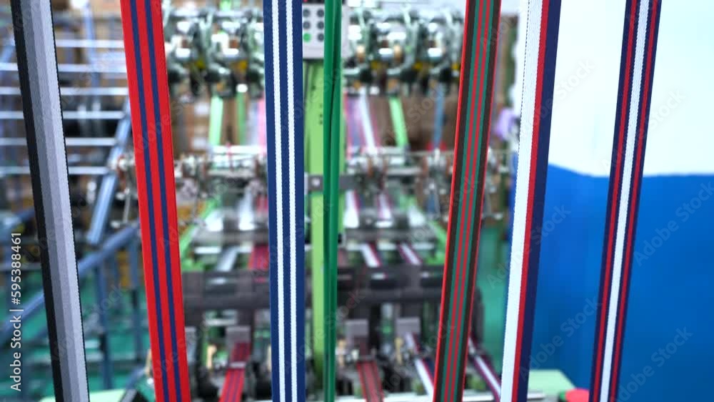 Thread from weaving machine. The mechanical equipment of the plastic weaving production line is running in a factory. Industrial narrow woven production line. Weaving looms in a textile factory. Thread from weaving machine. The mechanical equipment of the plastic weaving production line is running in a factory. Industrial narrow woven production line. Weaving looms in a textile factory.