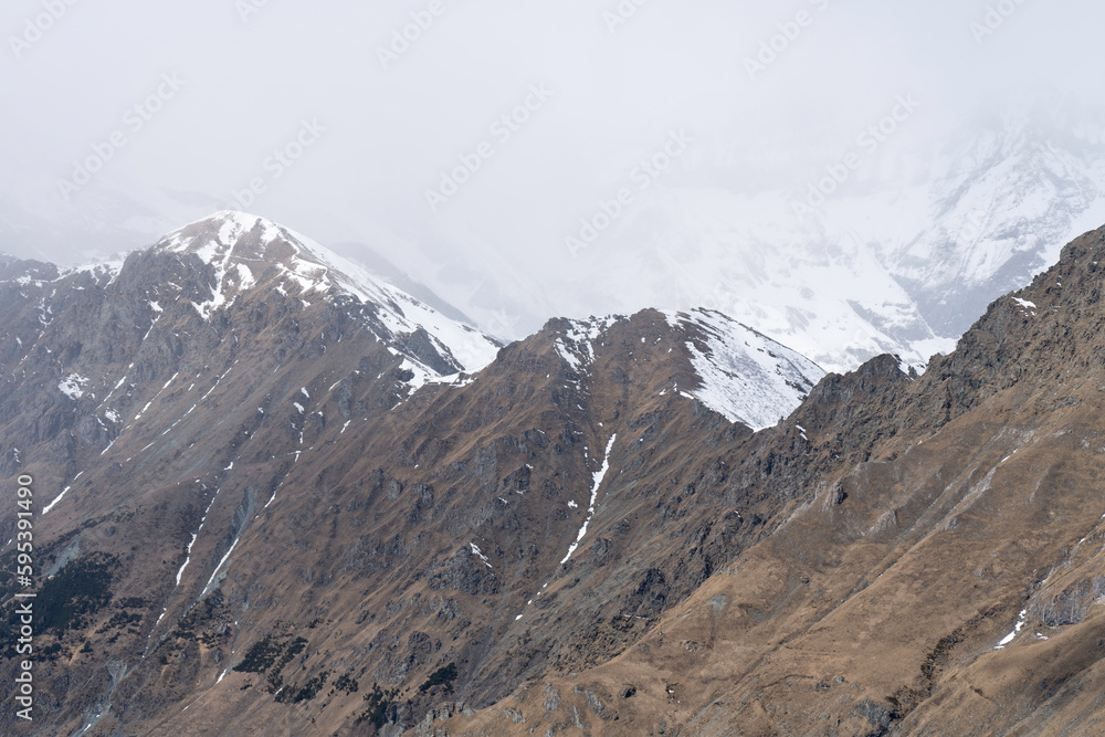 top of the rocky mountain ridge, snow covered mountains in the clouds background, snowy day