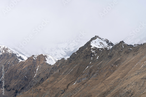 top of the rocky mountain ridge, snow covered mountains in the clouds background, snowy day