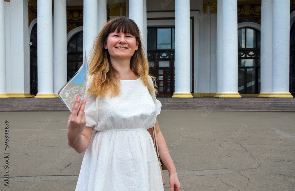 Smiling woman traveler in white dress with map at town street. Concept of travel, summer vacation, solo female tourism, adventure, trip, journey Smiling woman traveler in white dress with map at town street. Concept of travel, summer vacation, solo female tourism, adventure, trip, journey