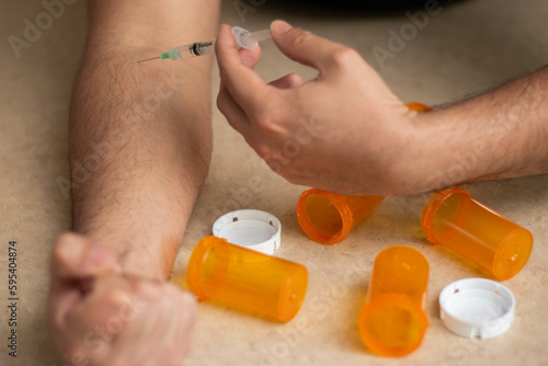 A person addict trying to self inject with a syringe and empty bottles of drugs around