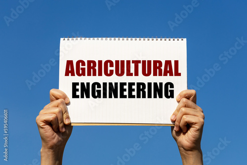 Agricutural engineering text on notebook paper held by 2 hands with isolated blue sky background. This message can be used as business concept about agricutural engineering. photo