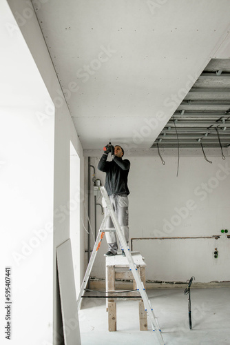Construction worker assemble a suspended ceiling with drywall and fixing the drywall to the ceiling metal frame with screwdriver. Renovation, construction and do it yourself DIY concept. © volody10