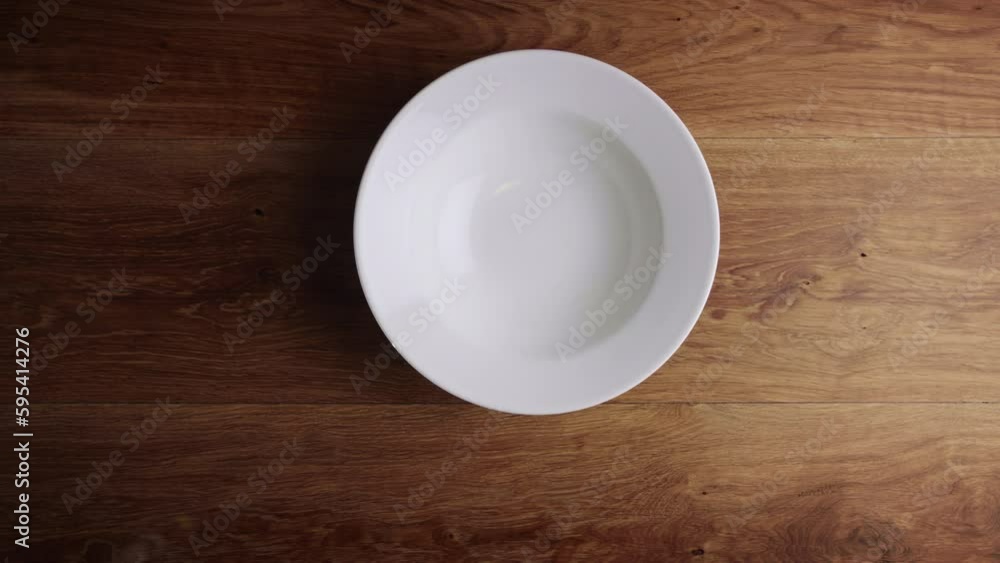 Top view of two male hands placing an empty white plate on a wooden surface. Top view of two male hands placing an empty white plate on a wooden surface.