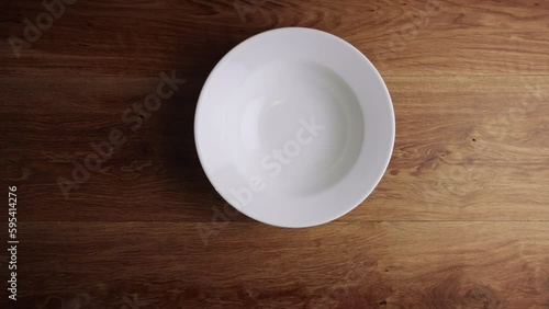 Top view of two male hands placing an empty white plate on a wooden surface.