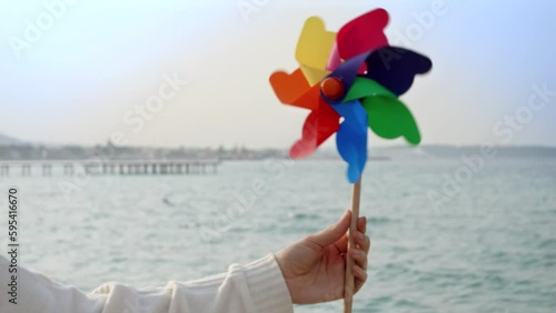 Young woman playing with a colorful spinning pinwheel on the sandy sea beach. Summer holiday, travel, and positive emotions photo