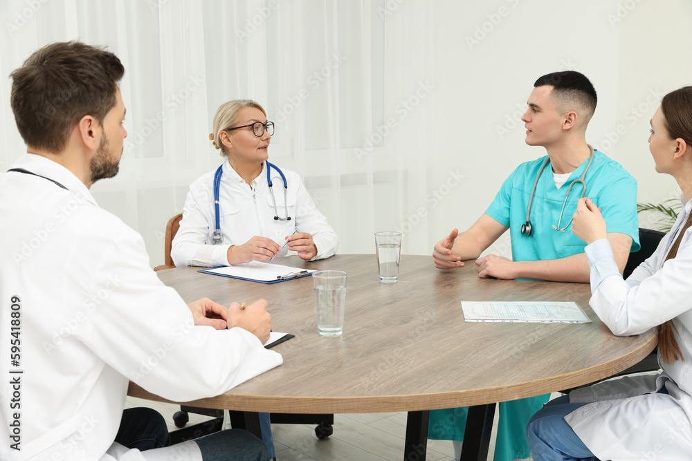 Medical conference. Team of doctors having discussion at wooden table in clinic Medical conference. Team of doctors having discussion at wooden table in clinic