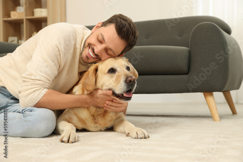 Man hugging his cute Labrador Retriever at home. Space for text