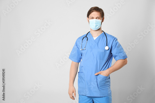 Doctor or medical assistant (male nurse) with protective mask and stethoscope on light grey background. Space for text photo