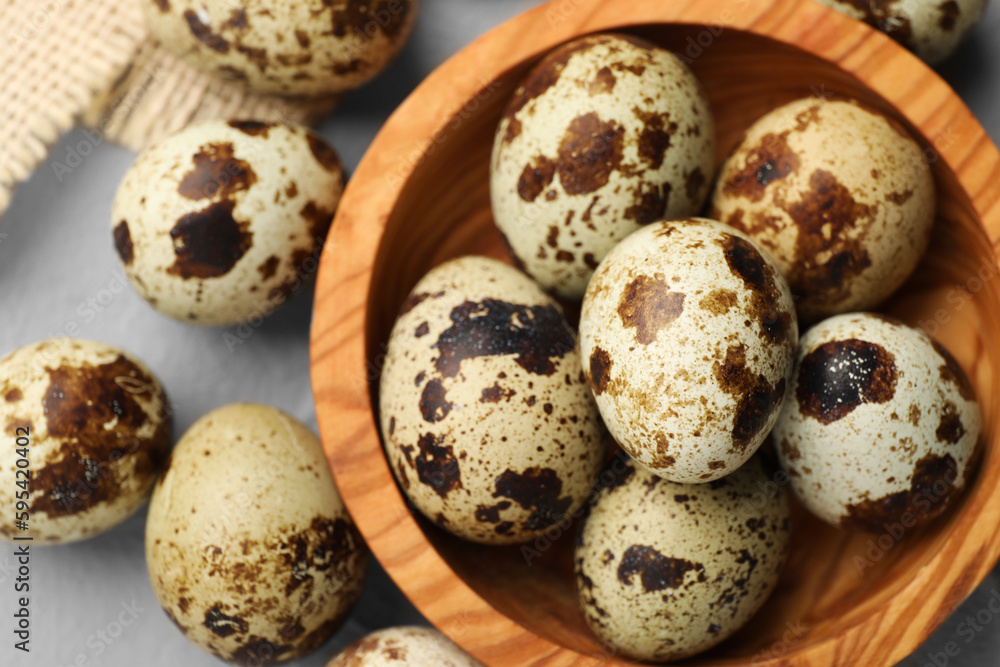 Wooden bowl and many speckled quail eggs on grey table, flat lay Wooden bowl and many speckled quail eggs on grey table, flat lay